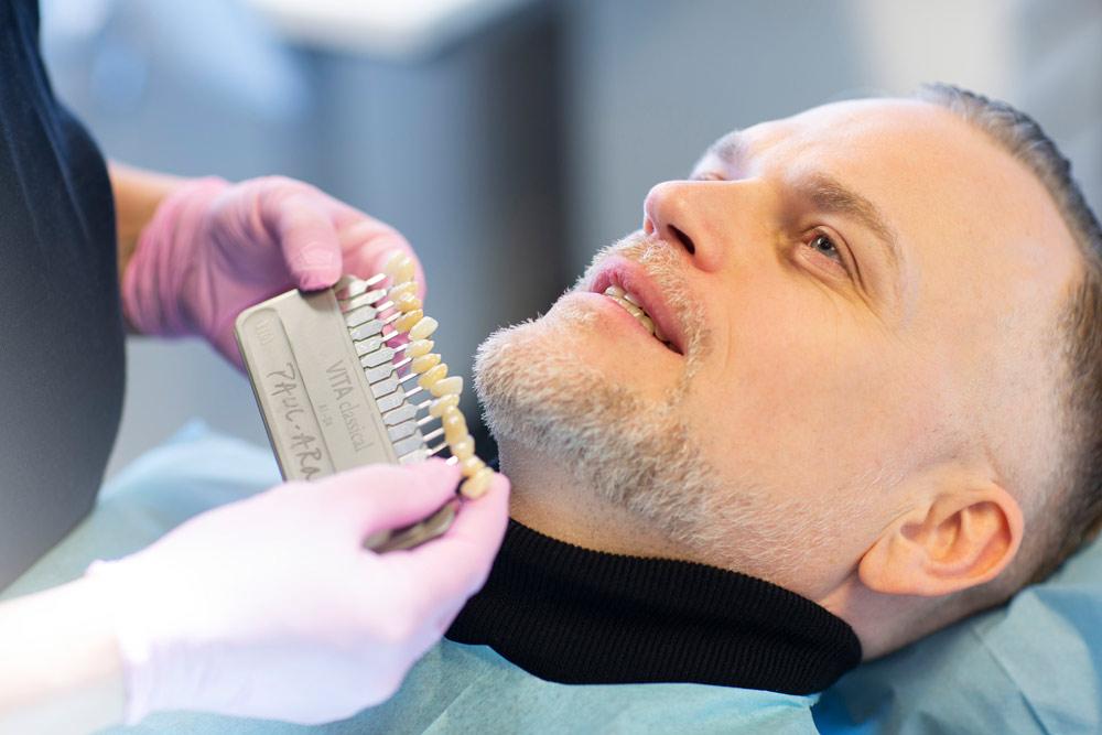 Tannlegen holder opp en fargepalett foran tennene til Anders, for å finne riktig farge til nye tenner.