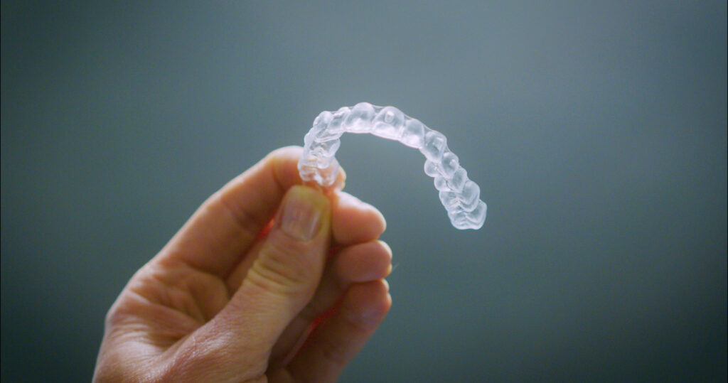 En hånd holder frem en skinne av typen gjennomsiktig tannregulering.